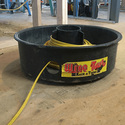 The Wire Tub by Rack-A-Tiers dispensing a yellow cable coil. It is sitting on the floor of a construction jobsite.