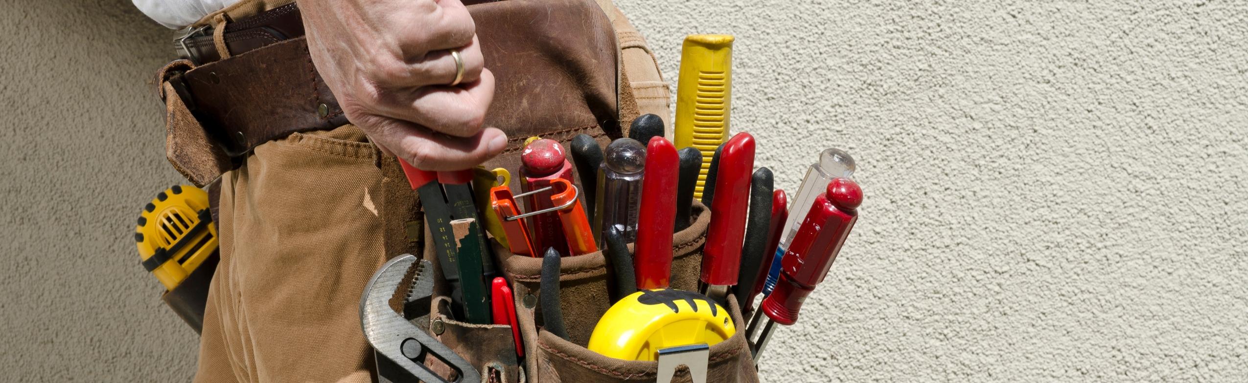 An electrician's tool pouch. It is full of tools including a tape measure, pliers, and screw drivers.