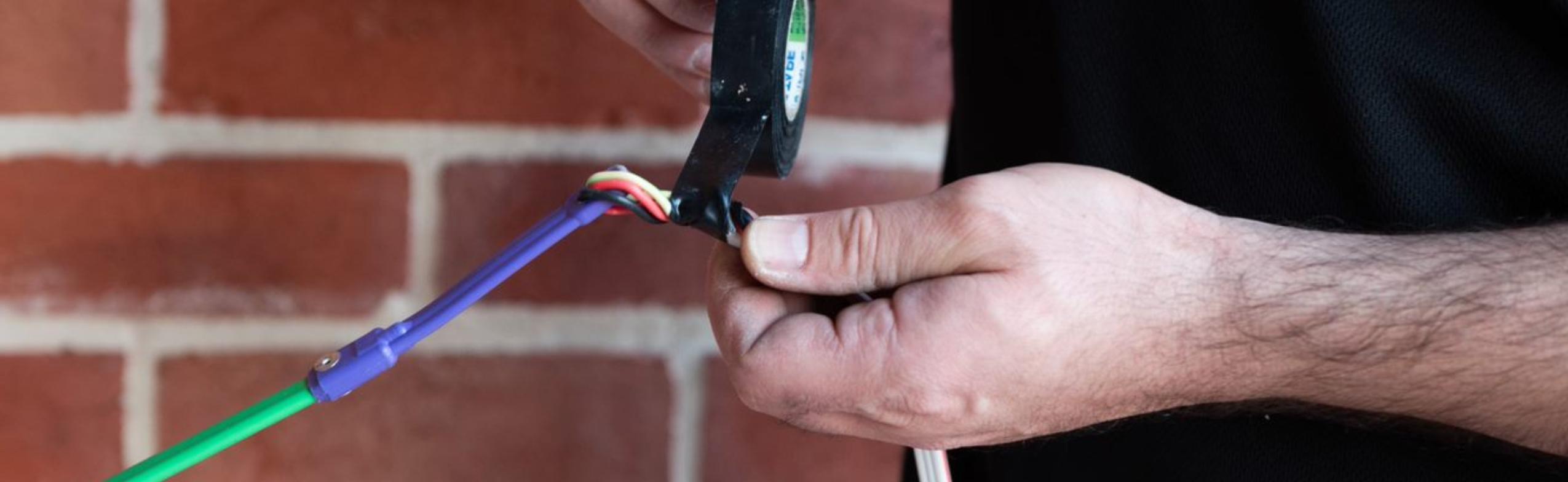 an electrician using electrical tape to attach a fish tape to a wire.
